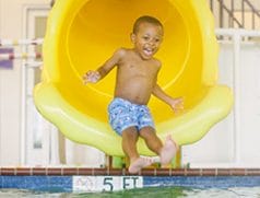 A boy coming out of a yellow slide into a pool