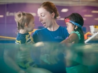 An instructor holding two children in the water as she teaches them to swim
