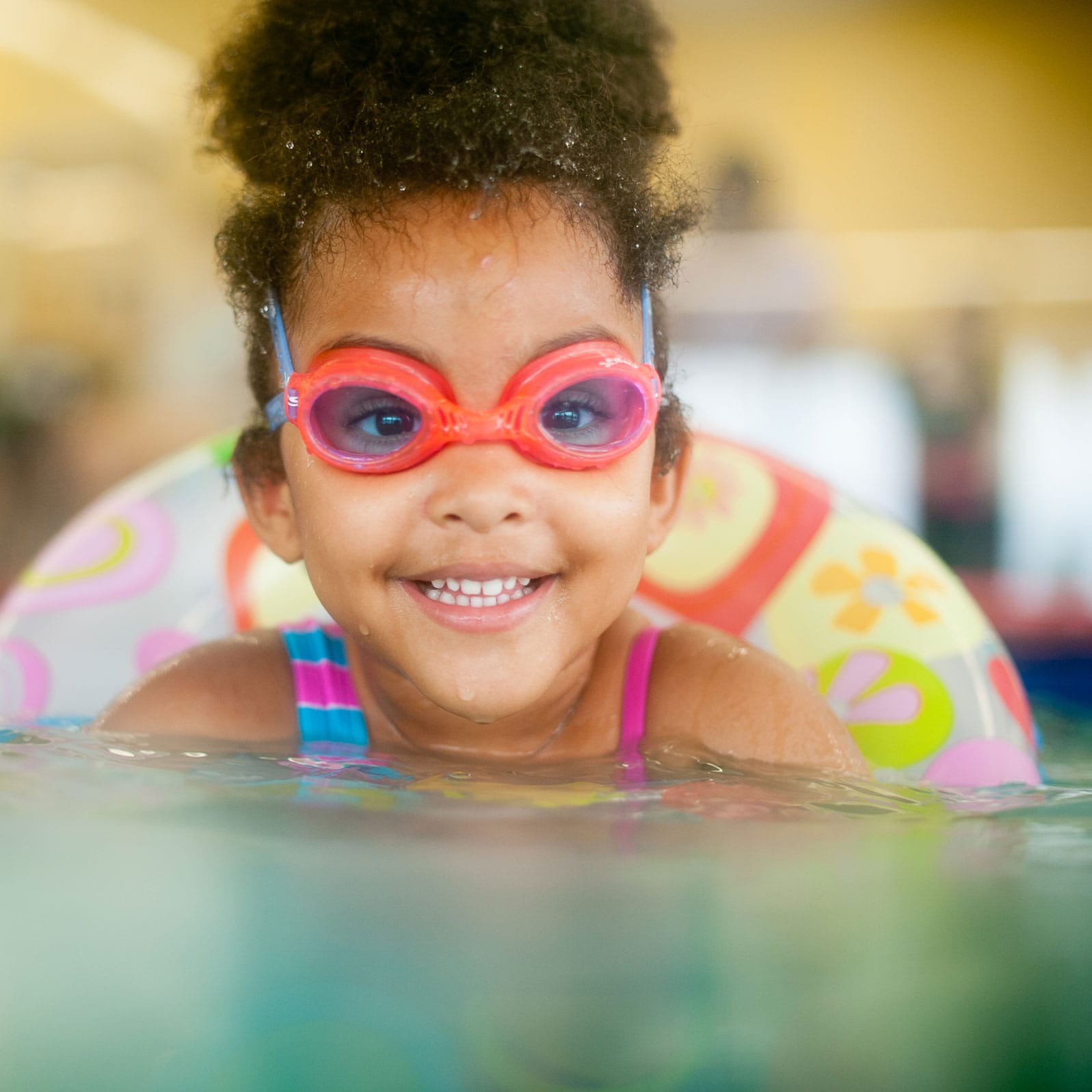 A smiling girl with googles and float tube around her waist swimming in a pool