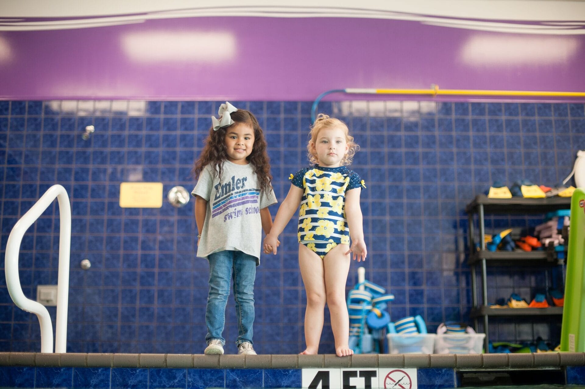 Two girls holding hands in front of a swimming pool at Emler's Fort Worth Swim School location