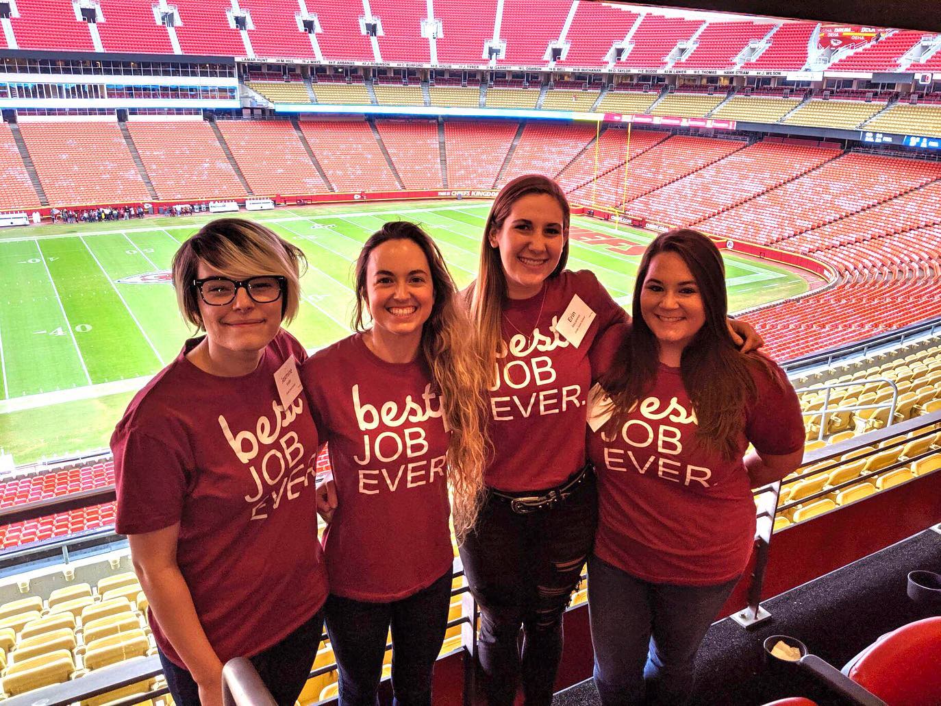 Four members of the Emler team at a Kansas City Chiefs game wearing red Best Job Ever shirts