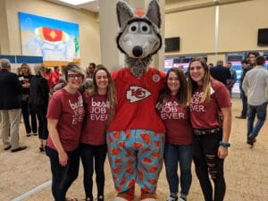 Four members of the Emler team with Kansas City Chiefs Mascot wearing red Best Job Ever shirts