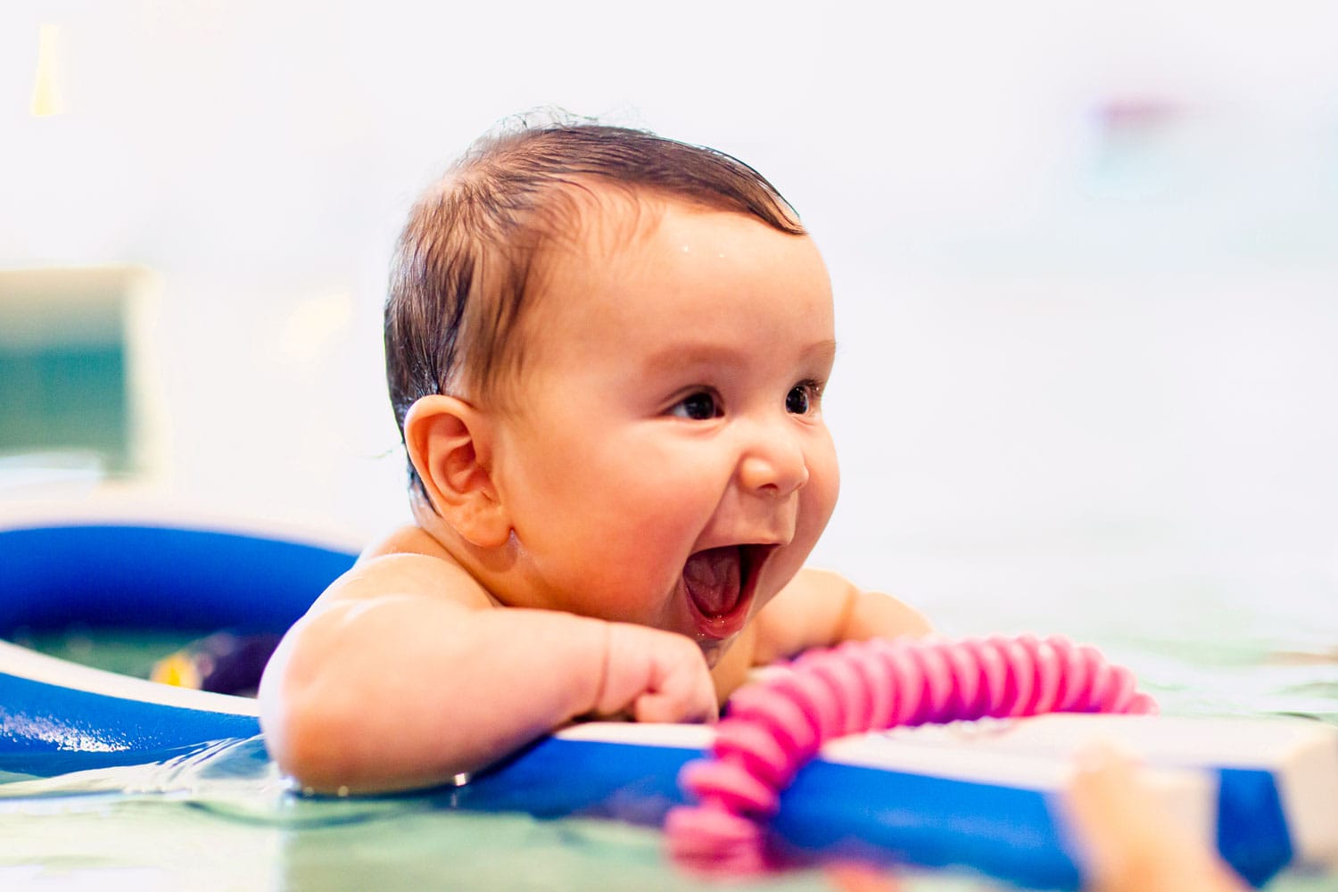 A Smiling baby in a floating ring learning to swim