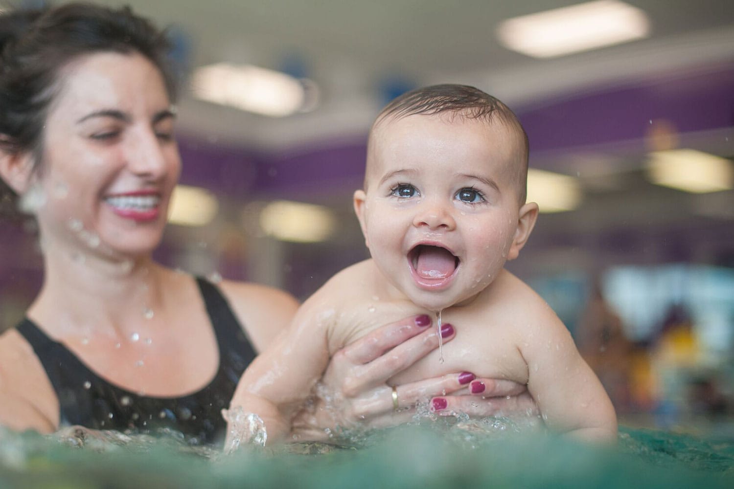 Mother holding a smiling baby boy in front of her in the pool