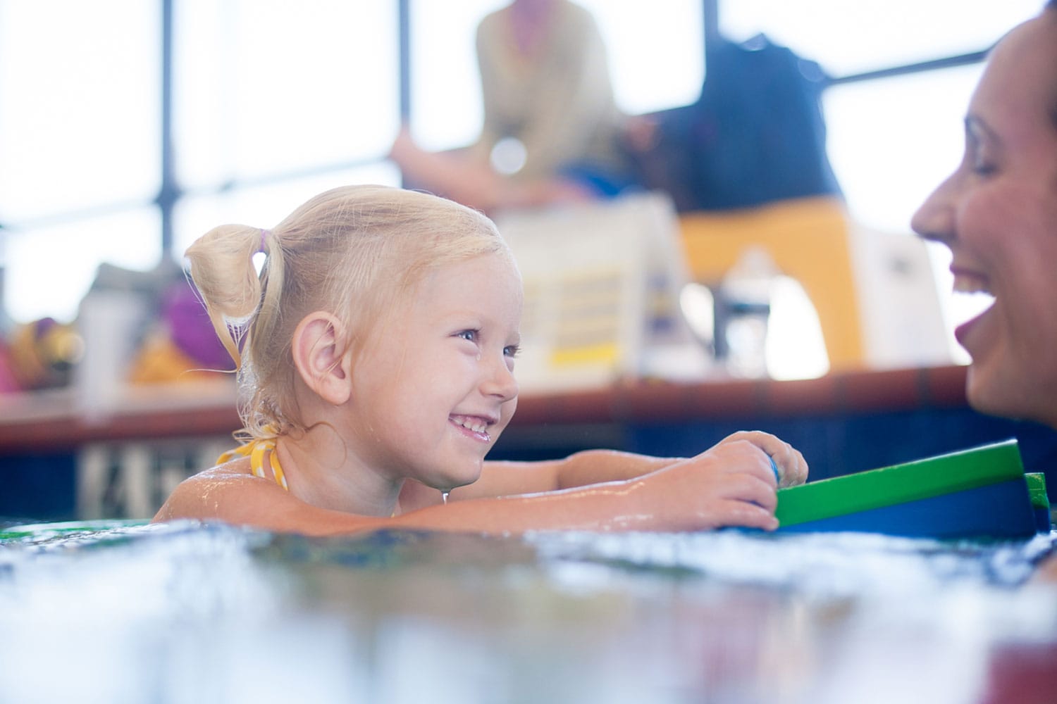 Smiling blonde girl holding a floaty learning to swim with her instructor