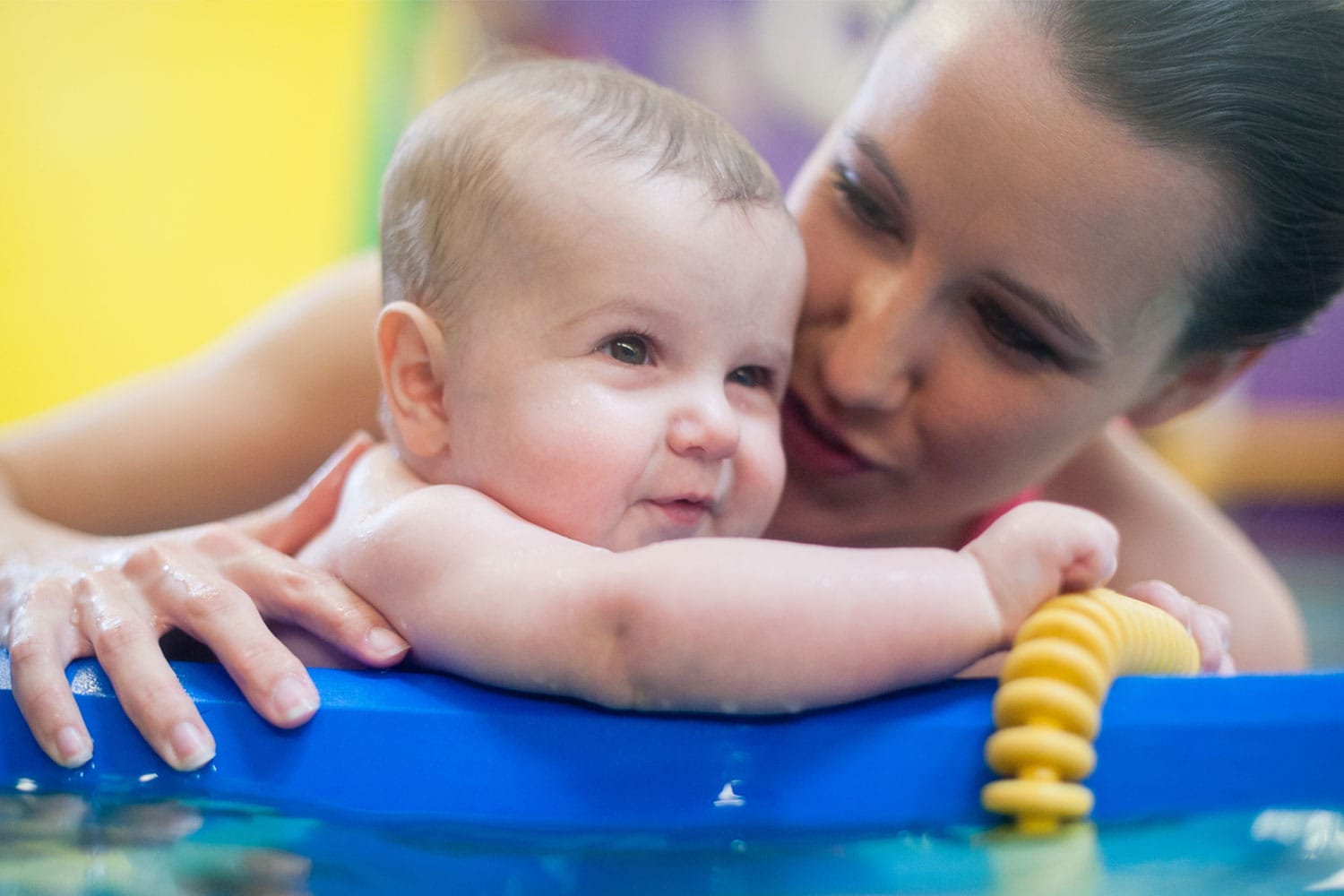A mother talks to a baby as they hold on to a floaty in the pool